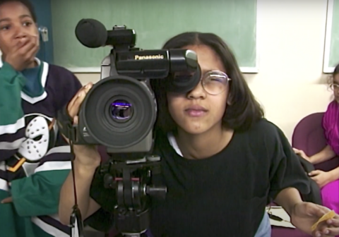 Young Reyna Bonaparte behind a video camera.