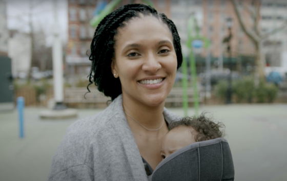 Woman in grey sweater holds baby and smiles