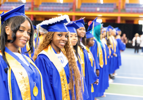 Teenagers in blue graduation uniforms standing in gynasium.