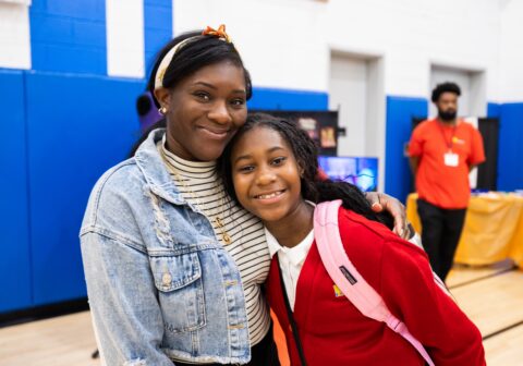 Female scholar and her mother smiling at the camera, posed for a photo in the gym.