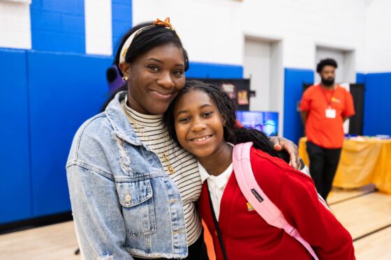 Female scholar and her mother smiling at the camera, posed for a photo in the gym.