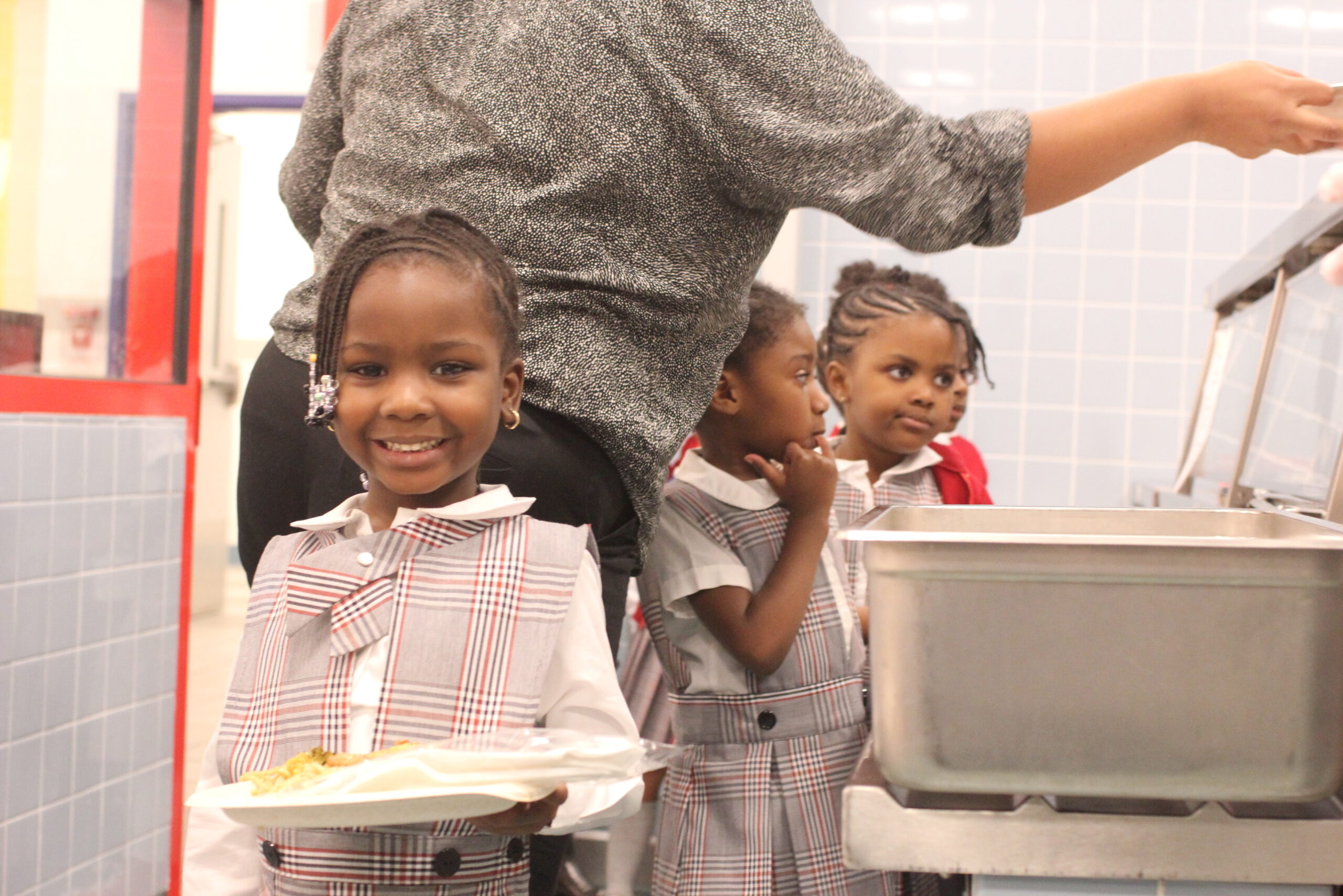 Young girl in HCZ Promise Academy school uniform hold a trey of healthy food in a cafeteria.