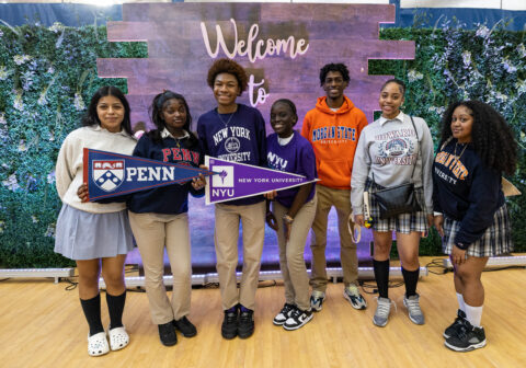 Harlem Children's Zone scholars wearing college attire and holding up college penants at National College Signing Day 2023
