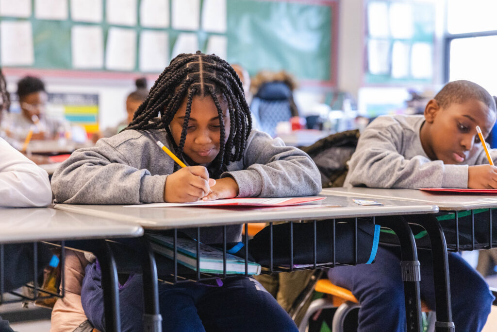 Scholars at their classroom desk completing a written assignment