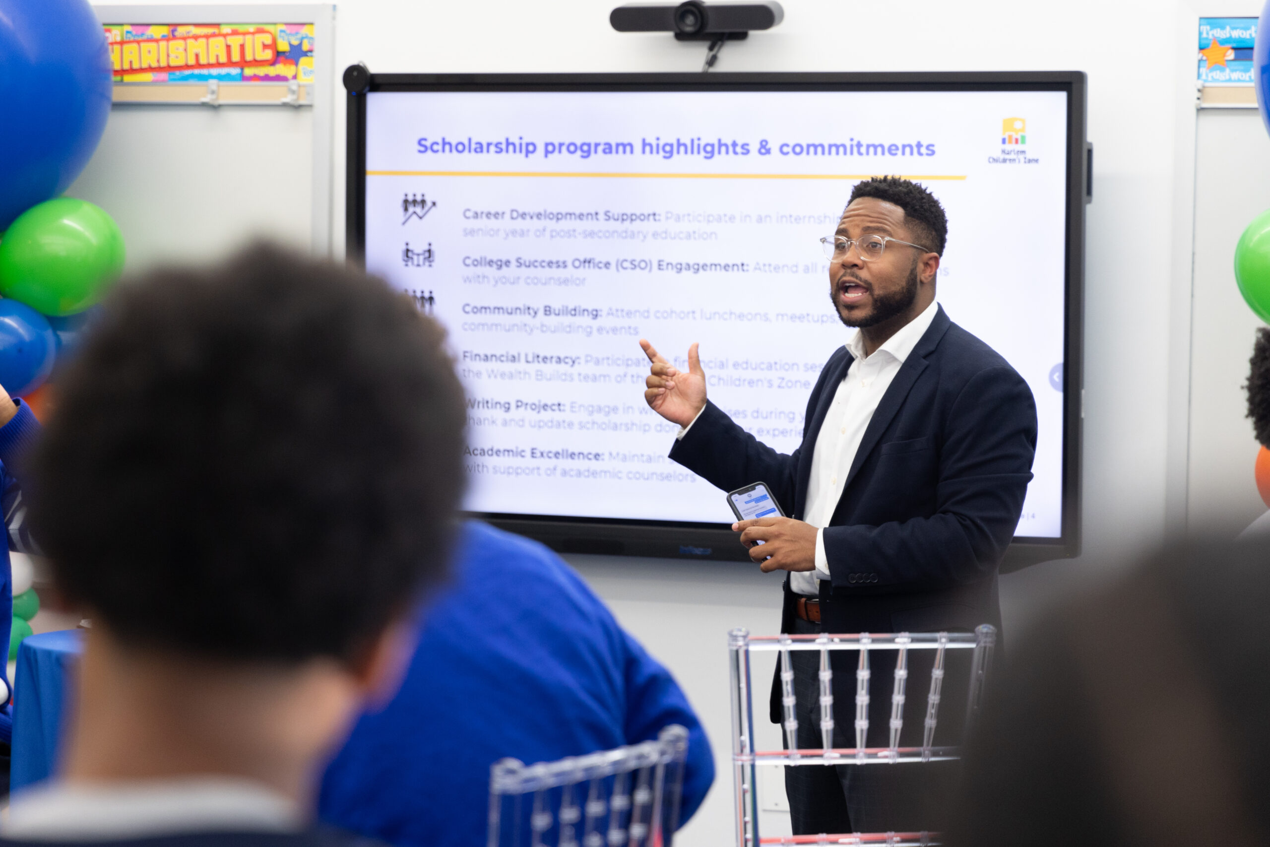 Man in black suit presents next to screen.