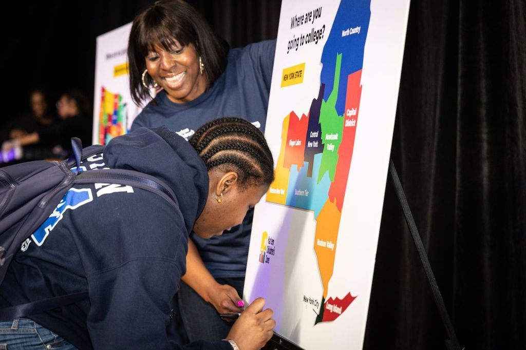 Harlem Children's Zone scholar in sweatshirt adds pin to national map to indicate where she will go to college.