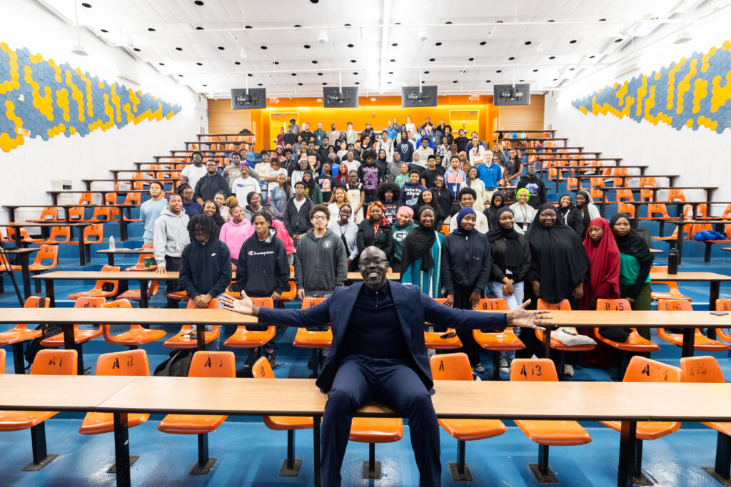 Kwame Owusu-Kesse poses with a group of teenage students in a college classroom.