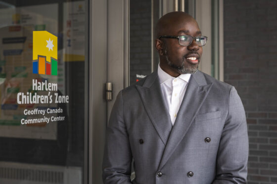 Kwame Owusu-Kesse stands outside a door emblazoned with the Harlem Children's Zone logo.