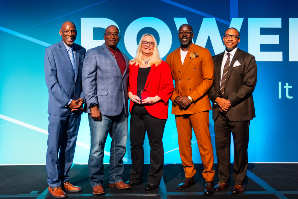 A woman stands on stage holding an award with four men