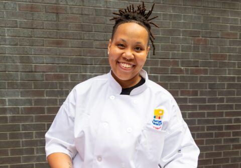 Chef in white chef jacket serves tray of food.