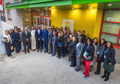 A group of mayors stands in front of a yellow wall outside the school building