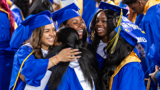 A group of female students in blue caps and gowns smile and hug each other.