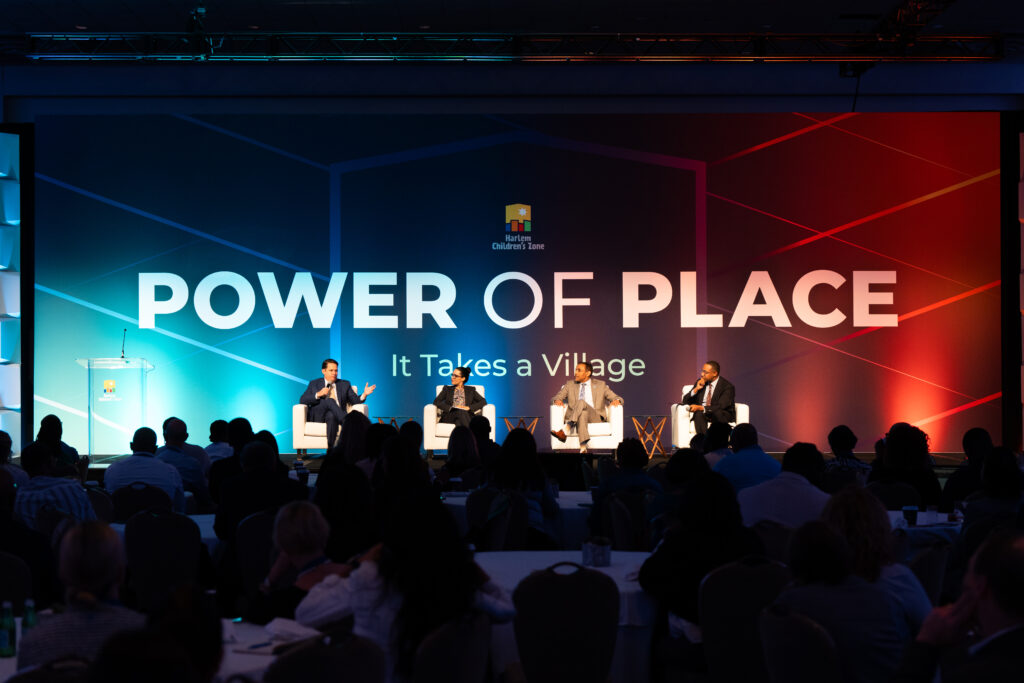 A panel of 4 professionals seated on a stage, in front of a crowd of other professionals.