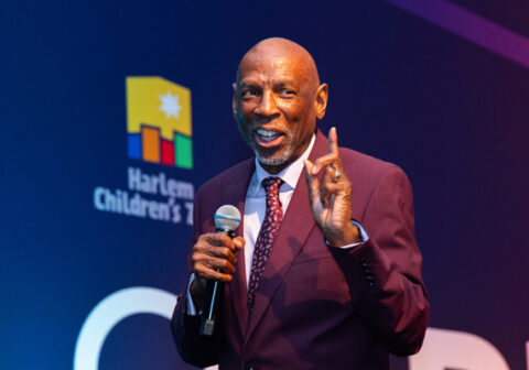 Man in maroon suit speaks on stage.