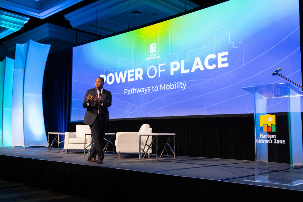 A man in a dark gray suit walks across the stage, giving a speech.