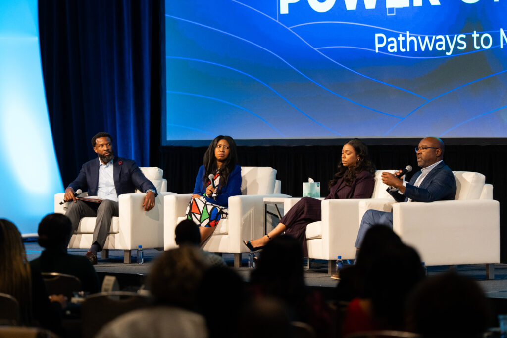 A panel two men and two women sit on stage having a discussion