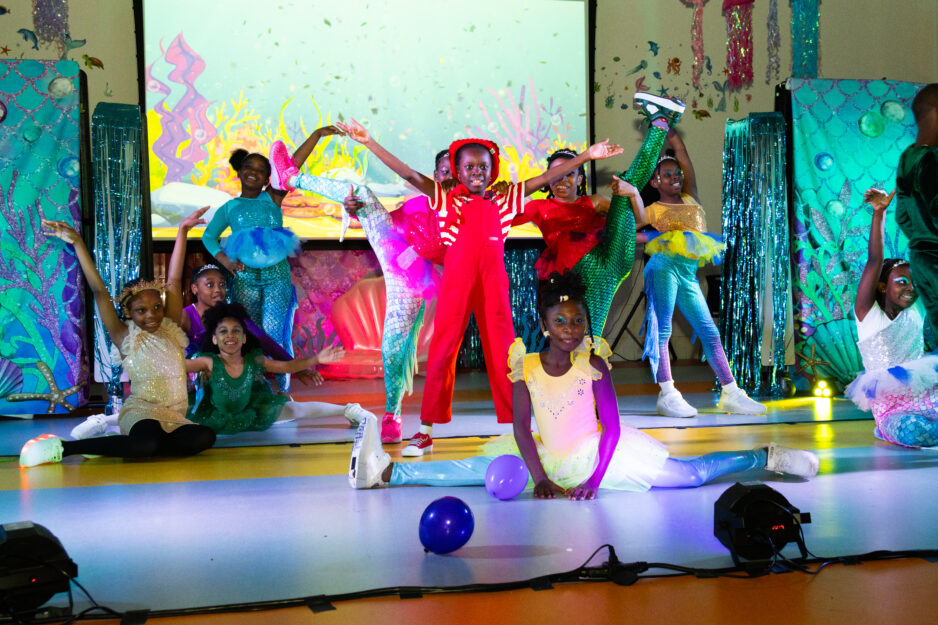 Young scholars perform on stage in little mermaid costumes.