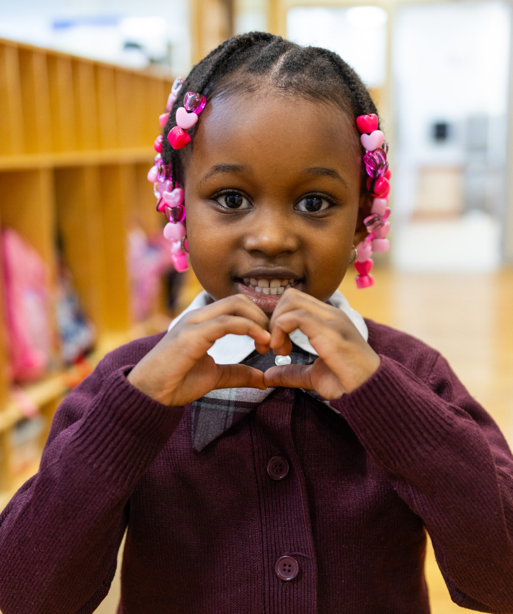 young female scholar holds up her hands to form a heart.