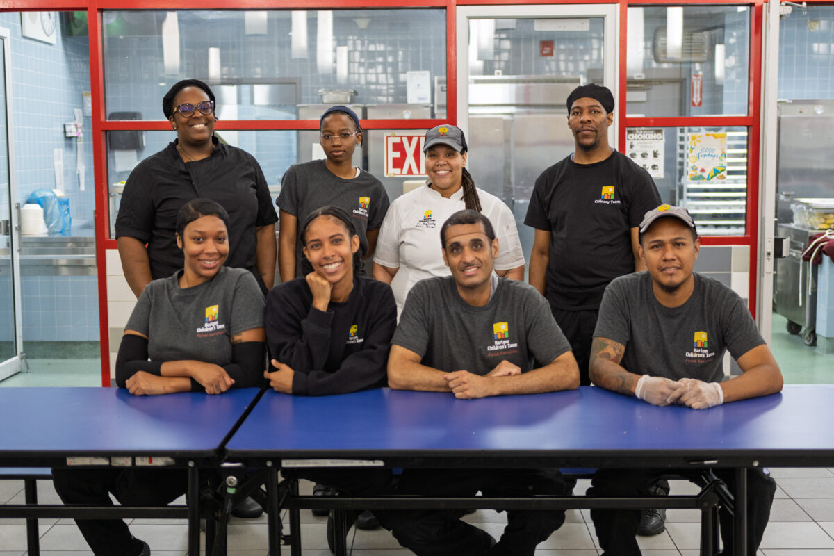 Eight food services professionals pose for a group picture in the cafeteria.