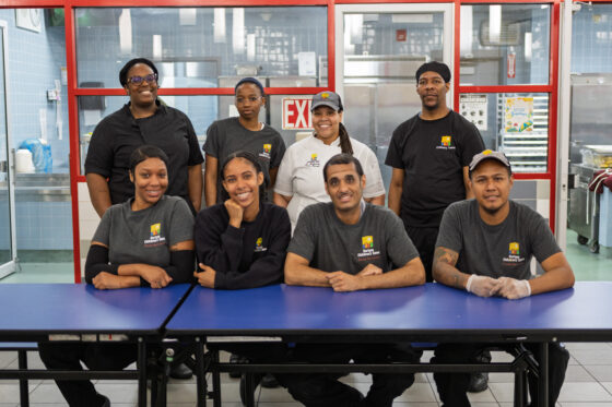 Eight food services professionals pose for a group picture in the cafeteria.