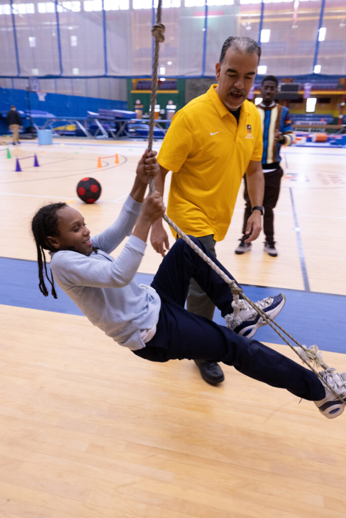 Young male scholar swings on a rope in a gym.