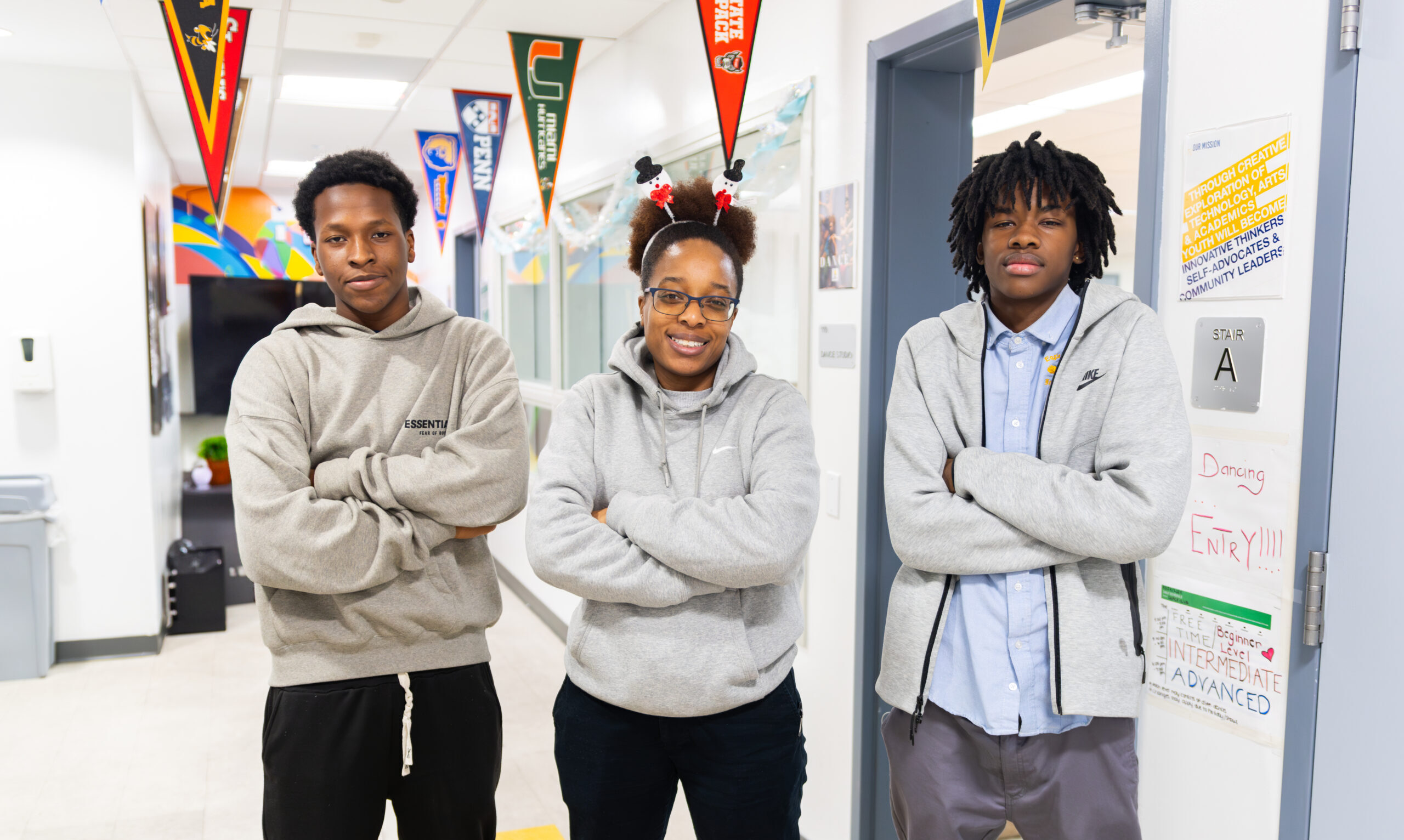 3 people posing for a photo with their arms crossed in a school hallway.