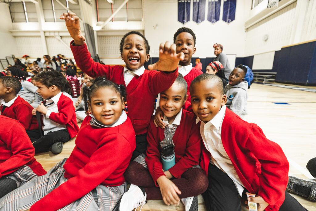 Children in red uniforms smile in gymnasium.