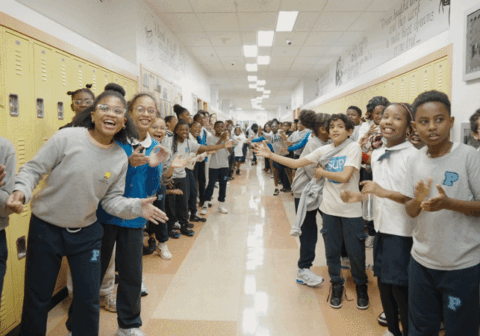 Children in school hallway clap and jump.