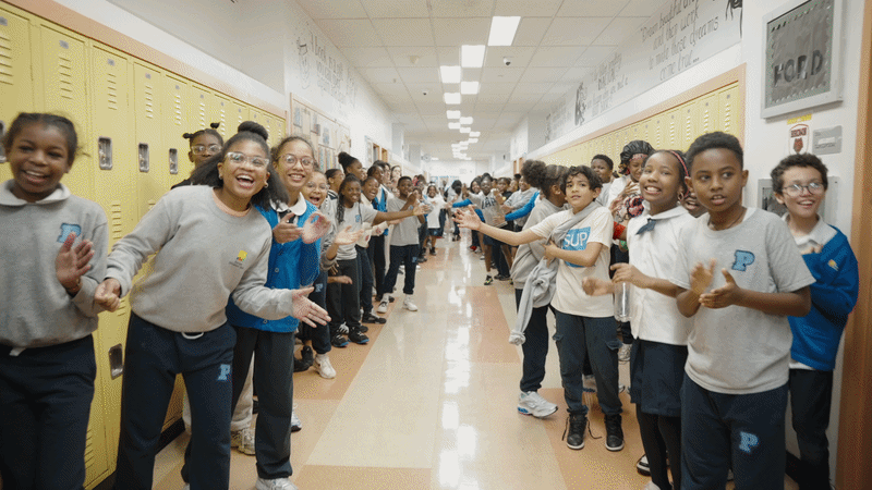 Children in school hallway clap and jump.