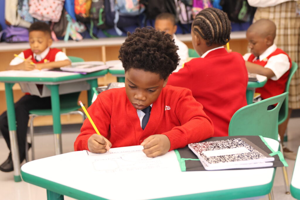 A scholar in a red sweater sits at a desk.